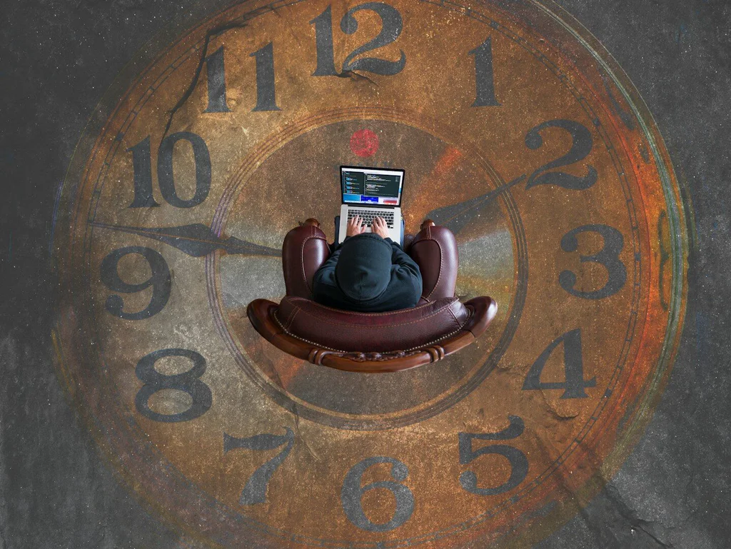 A person in a hoodie typing on a laptop in a leather armchair