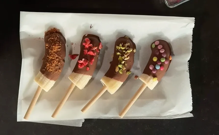 Banány nařežeme na špalíčky a napíchneme na špejli, polijeme čokoládou a zdobíme.