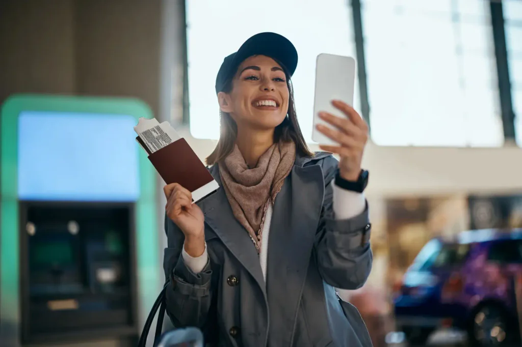 Žena na letišti, která se těší na dovolenou a sleduje něco na telefonu.