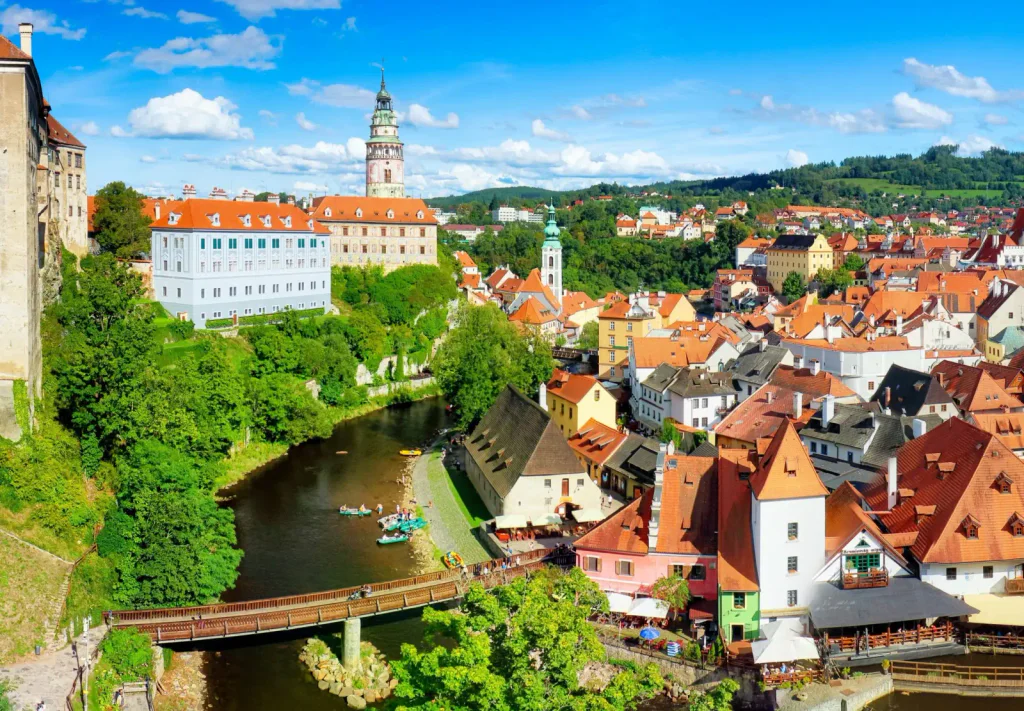 Letecký záběr na Český Krumlov. Vidět jde nalevo zámek, vedle něj řeka s mostem a na pravé straně město.