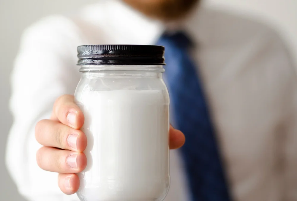 Muž ukazující uzavřenou sklenici s mlékem
