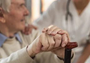 Starý muž se opírá o hůl a mluví s lékařem