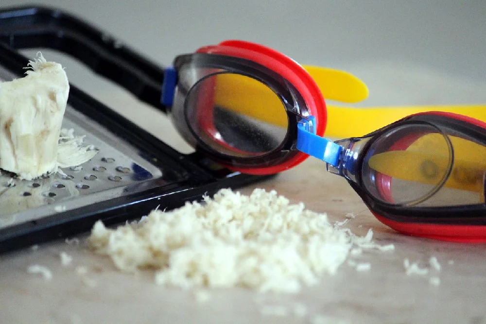 Strouhaná hromádka křenu se struhadlem a plaveckými brýlemi proti pálení očí