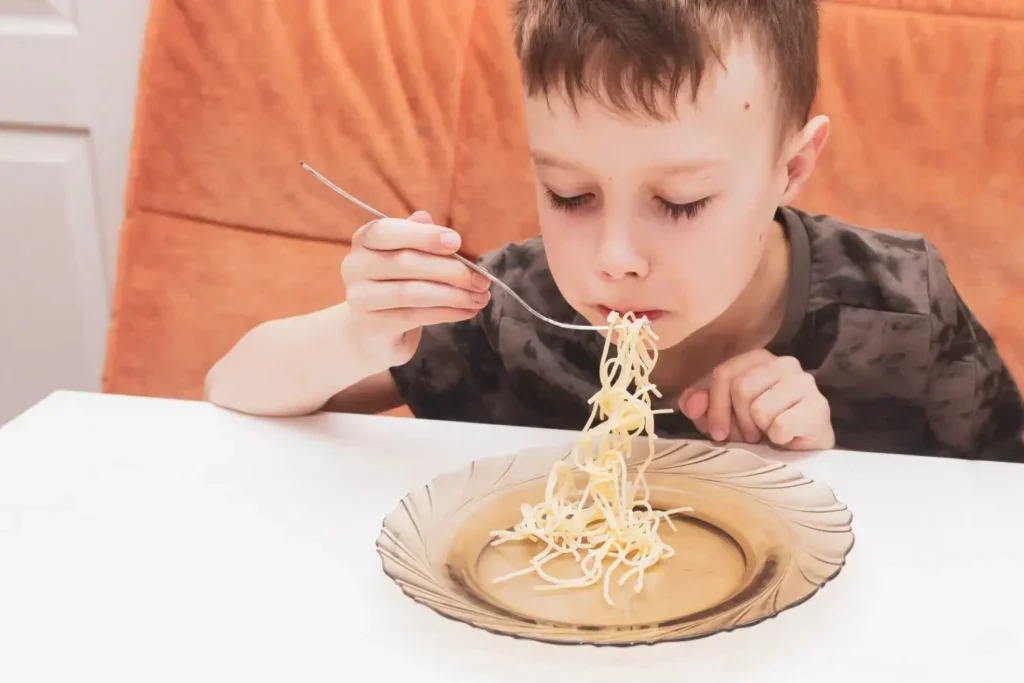Malý chlapec obědvá suché těstoviny
