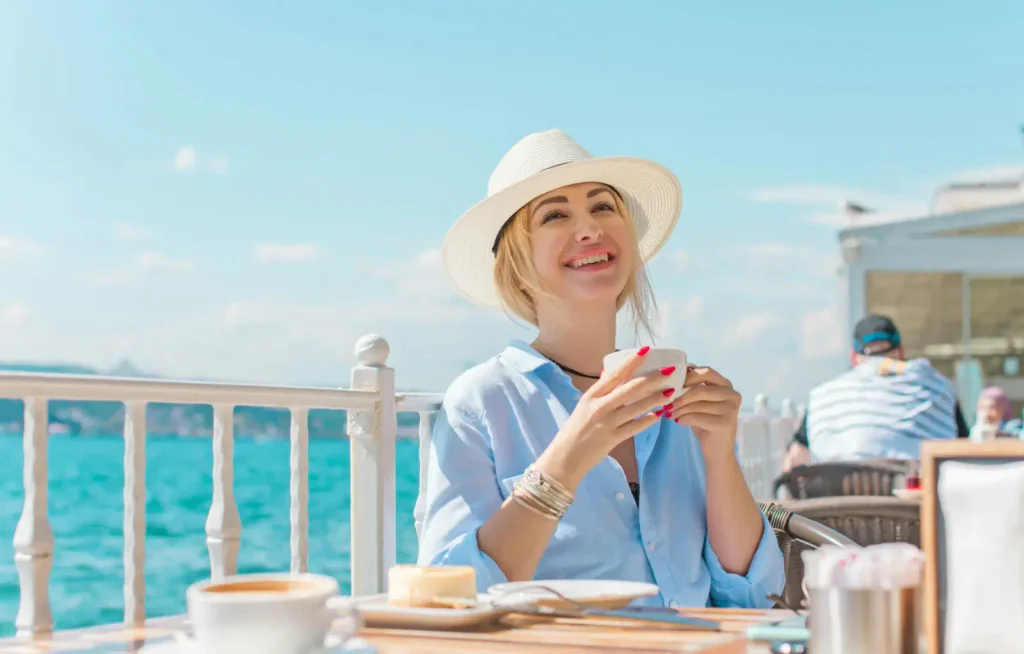 Blondýna si v kloboučku užívá snídani ráno u moře 
