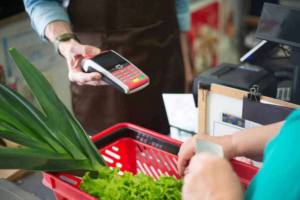 A customer using a contactless payment method at a grocery store checkout with fresh produce.