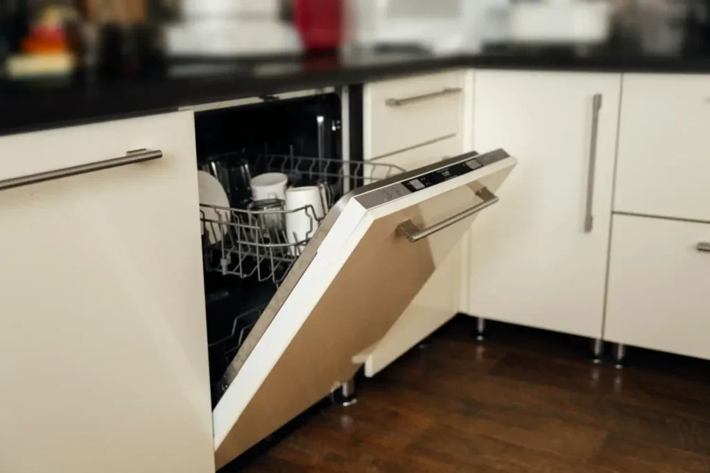 Otevřená myčka v bílé kuchyni plná nádobí