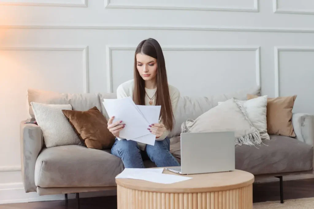 Žena sedí doma na pohovce a prohlíží si papíry