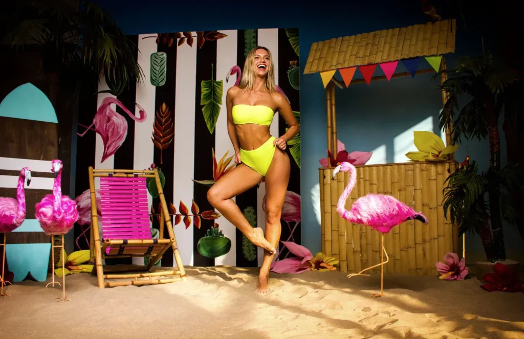 žena stojí na jedné noze mezi plameňáky